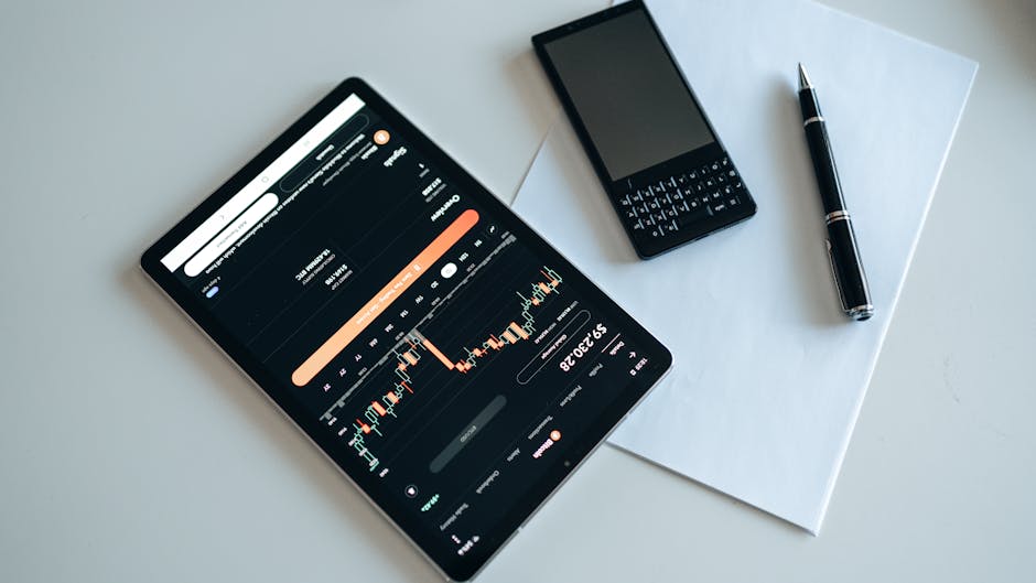 Top view of a workspace with a tablet displaying financial charts, a smartphone, pen, and paper.
